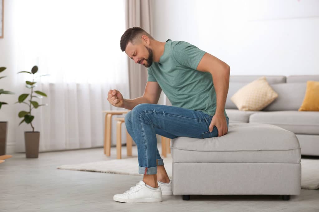 Man sitting on couch ottoman in pain