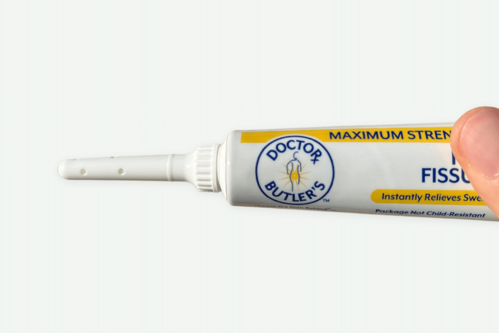 Image of a hand holding a tube of hemorrhoid cream with the applicator attached